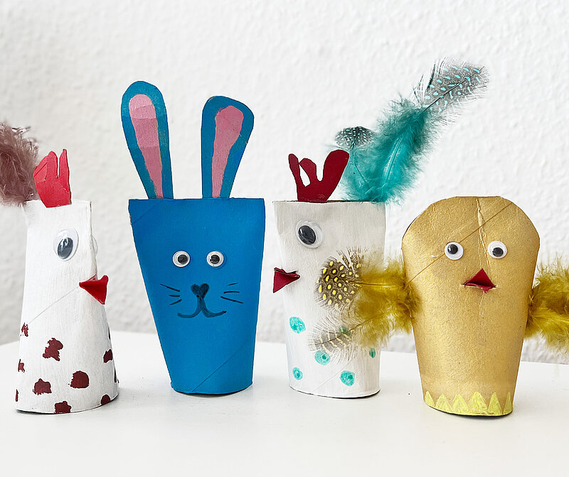 selbst gebastelte Osterdeko aus leeren Papprollen in Form von buntem Hasen, Kueken und Haehnchen