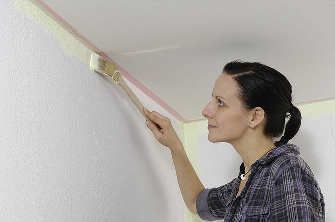 Wände richtig streichen – präzises Streichen der Kanten mit Pinsel entlang der abgeklebten Decke für exakte Farblinien