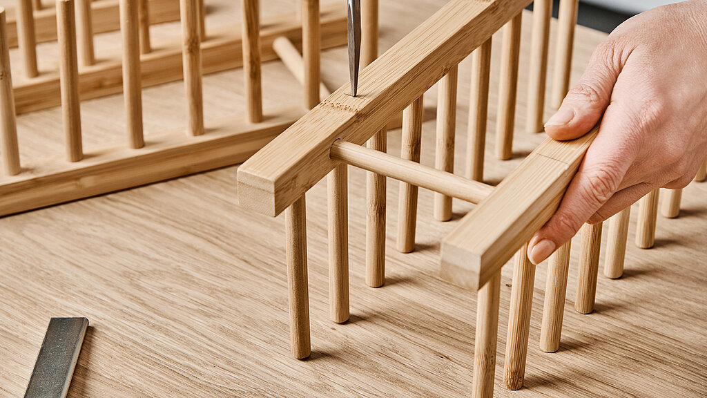 Küchenregal aus Tellerhaltern bauen mit vorbereiteten Holzstäben, Person setzt Holzleisten und Tellerhalter-Elemente zusammen, präzise Montage für ein stabiles und dekoratives Küchenregal