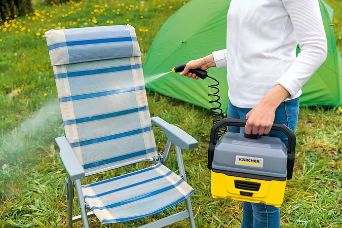 Mann säubert einen Camping-Klappstuhl mit einem Niedrigdruckreiniger