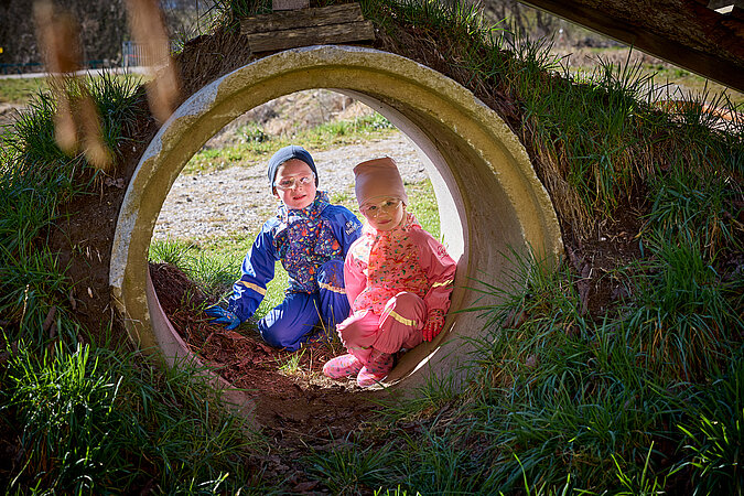 Tipps zum Heimwerken mit Kindern: Zwei Kinder sitzen in einem großen Betonrohr auf einem Abenteuerspielplatz – kreative DIY-Spielumgebung für Entdecker und kleine Baumeister.