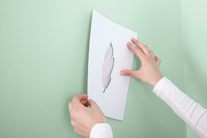 Auf eine grüne Wand wird mit Schabloniertechnik ein Blatt getupft