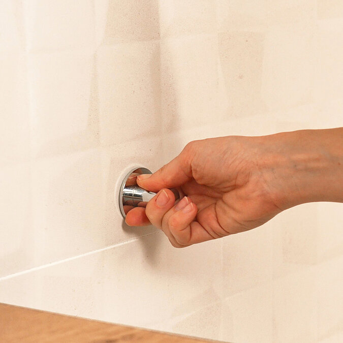 Handtuchhaken mit aufgetragenen Kleber "fix & ab" wird an der Wand, auf Fliesen angedrückt
