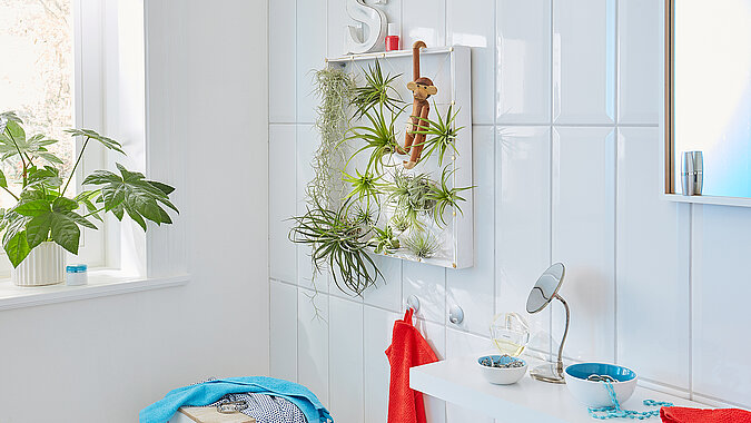 Wanddeko mit Pflanzen aus hängenden Gläsern am Fenster, kreative DIY-Idee mit Grünpflanzen und Glasbehältern als natürliche Wand- und Fensterdekoration
