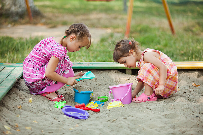 zwei kleine Mädchen in Sommerkleidern spielen in einem Sandkasten