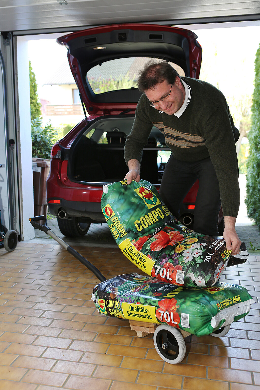 Mann hebt Säcke Blumenerde aus dem Auto und legt sie auf einen selbstgebauten Pflanzenroller