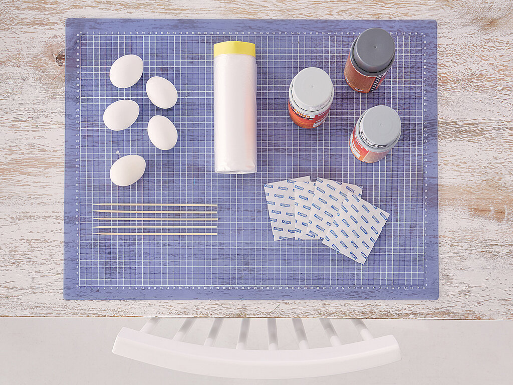 0stereier färben mit einfachen Materialien wie weißen Eiern, Papiertüchern, Sprühlack, Gummibändern und Holzstäbchen auf einem Basteltisch vorbereitet