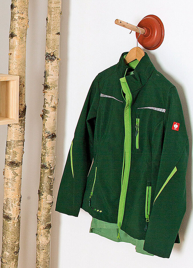 Arbeitsjacke hängt an einem Haken aus einem Pömpel am Raumteiler aus Birkenstämmen