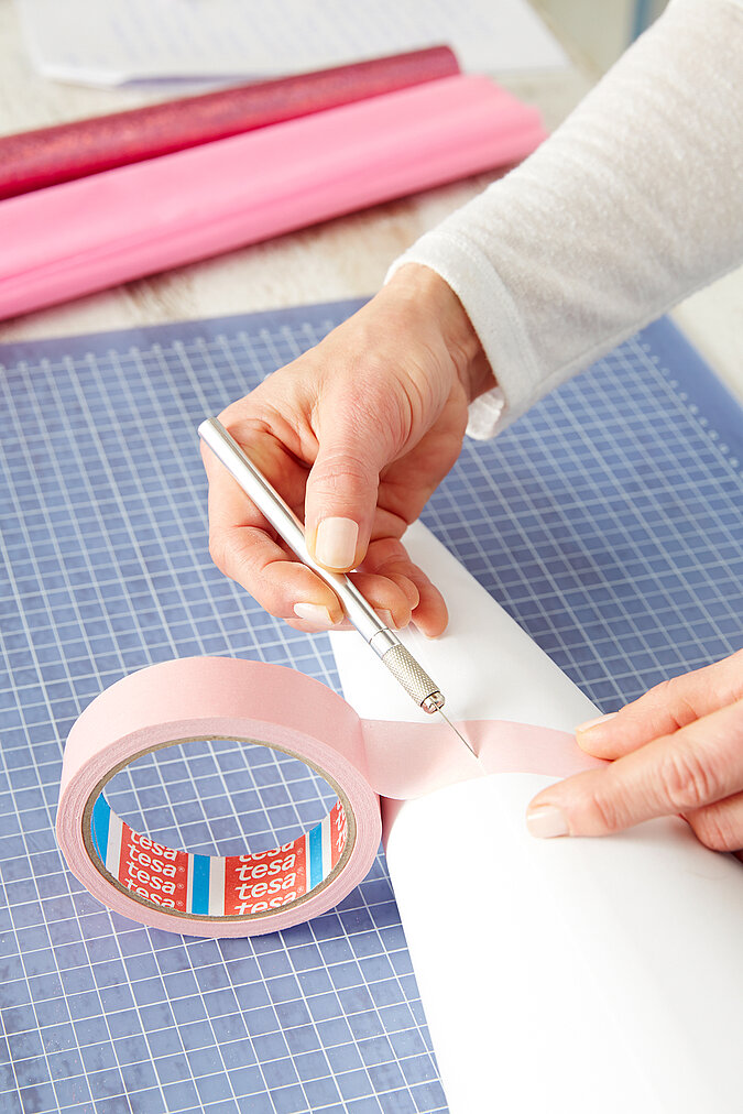 Auf einen weißen Schultüten-Rohling werden rosa Malerkrepp-Streifen für den Einhorn-Look geklebt