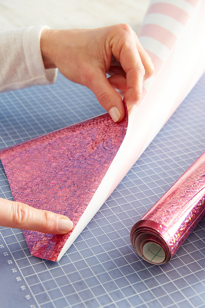 Eine Schultütenspitze wird mit rosafarbener, glitzernder Halogrammfolie beklebt