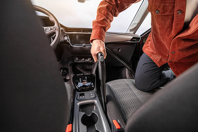 Auto selbst waschen und Innenraum reinigen – Mann saugt zwischen Mittelkonsole und Autositzen gründlich aus, um Staub, Krümel und Schmutz aus dem Innenraum zu entfernen.