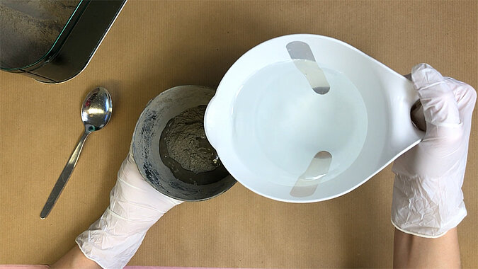 Türstopper aus Beton selber machen – Silikonform mit Ausgießöffnung wird über eine mit Beton gefüllte Form gehalten, Vorbereitung zum sauberen Abdecken des Gussmaterials
