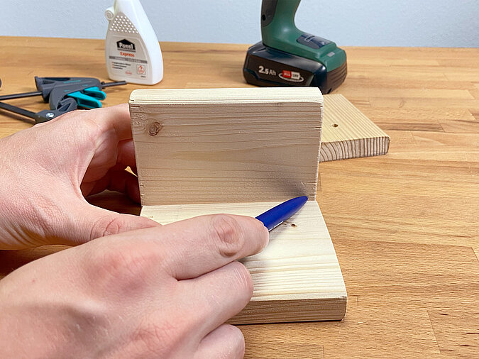 Markierung eines Bohrlochs an zwei rechtwinklig verleimten Holzstücken als Basis für ein Podest für eine DIY LED-Tischleute aus Getränkedose.