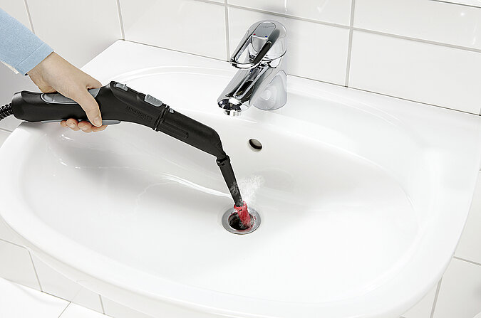 Duese eines Dampfreinigers wird per Hand zur Reinigung in einen Abfluss gehalten
