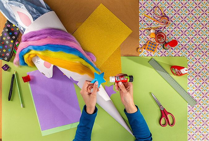 Schultüte Einhorn basteln beim Aufkleben von bunten Sternen zur Dekoration der Schultüte