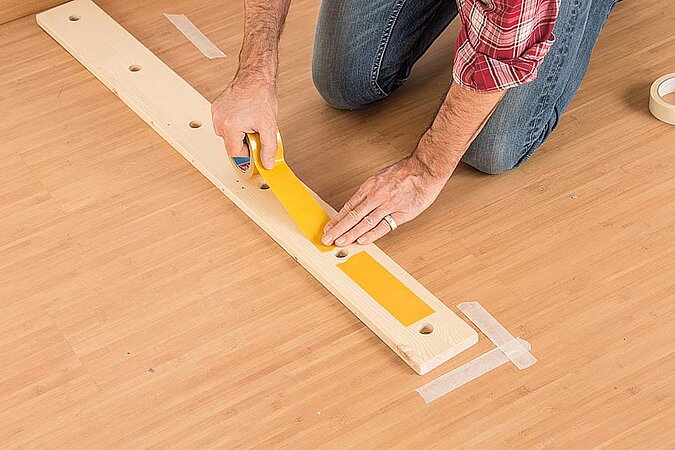 Doppelseitiges Klebeband wird auf das untere Holzbrett für den Raumteiler aus Birkenstämmen geklebt