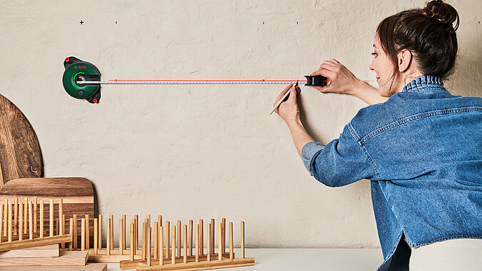Küchenregal aus Tellerhaltern bauen mit exakter Ausrichtung, Person überprüft die horizontale Linie an der Wand zur perfekten Montage eines DIY-Küchenregals