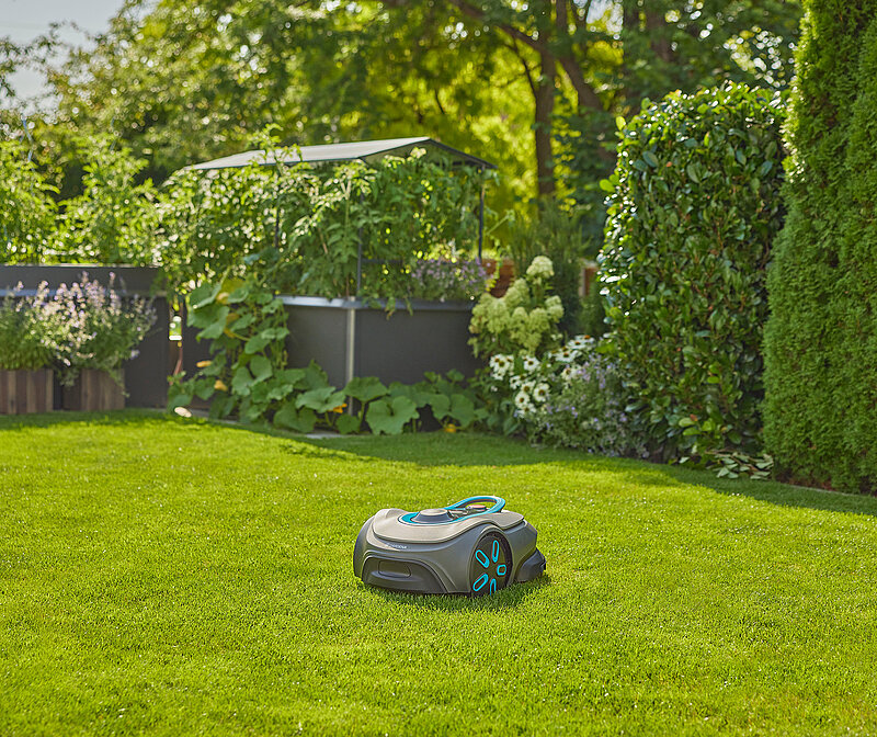 Mähroboter fährt autonom über den Rasen in modernem Garten mit Terrasse im Hintergrund