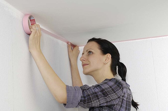 Wände richtig streichen – Abkleben der Deckenkante mit Malerkrepp für saubere Übergänge zwischen Wand und Decke