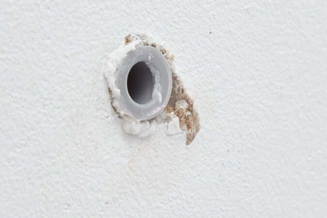 Weiße Wand mit einem Dübel in einem Bohrloch, der Dübel wurde zuvor mit Reparaturvlies umwickeltlies aushärten