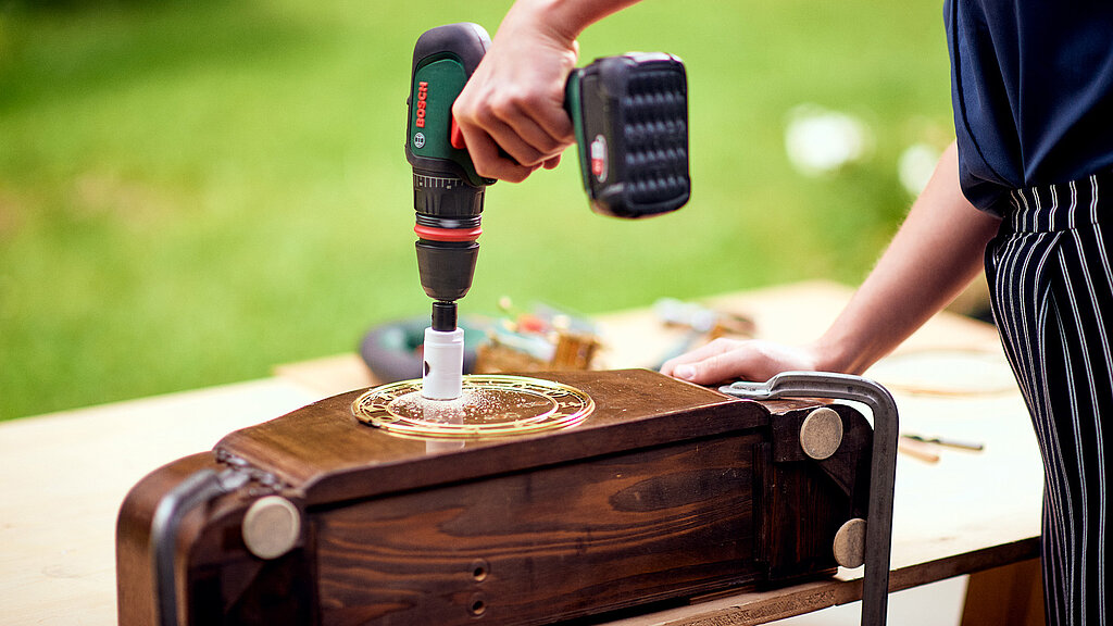 Upcycling-Idee Nistkasten aus Uhr bauen – Bohren der Einflugöffnung in ein altes Holz-Uhrengehäuse mit Akkuschrauber, DIY-Arbeitsschritt zur Vorbereitung eines Nistkastens aus einer Uhr