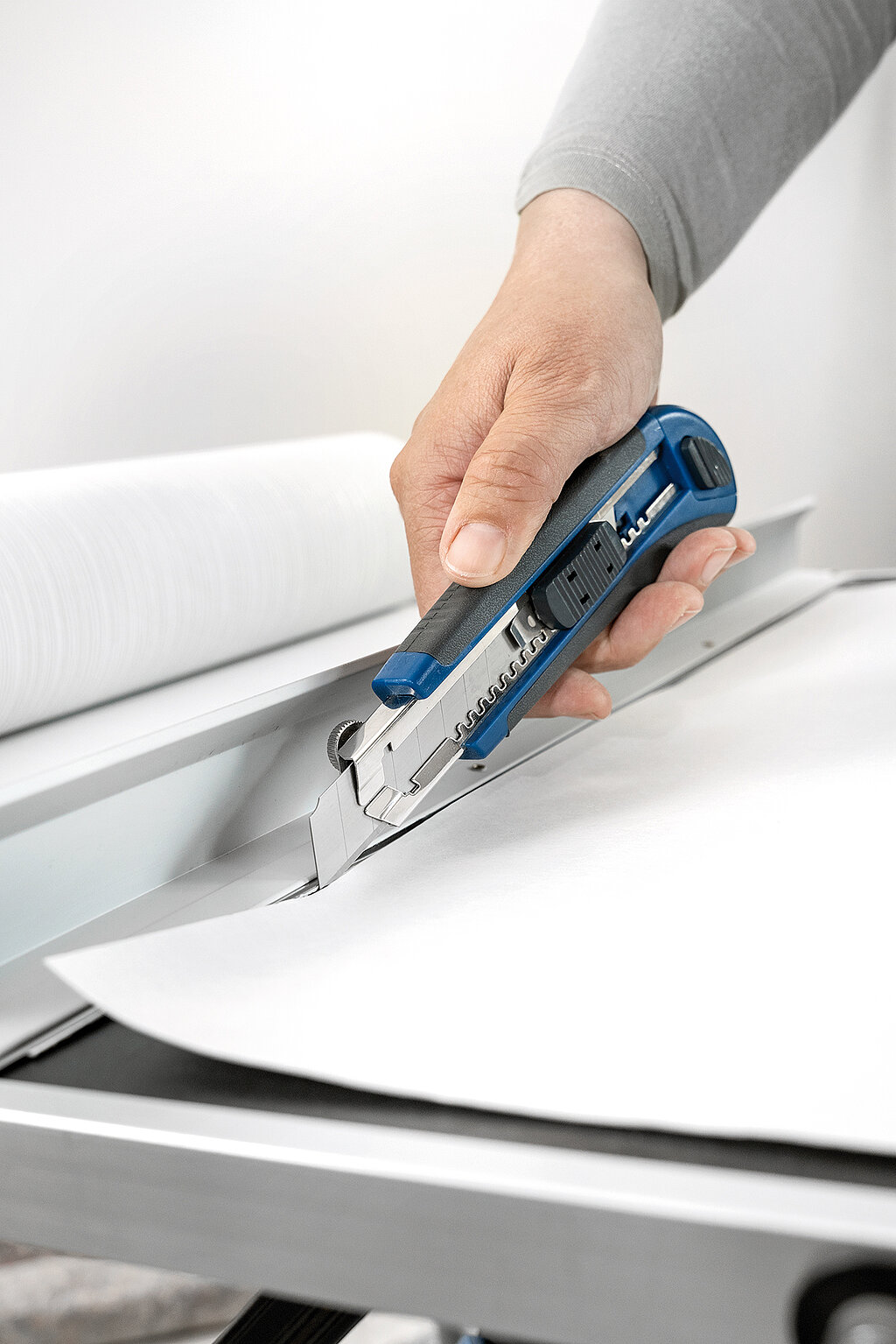 Wände richtig tapezieren – praktische Tipps zur Tapetenzuschnitte: Hand schneidet mit einem Cuttermesser präzise eine Tapetenbahn auf einem Tapeziertisch zu.
