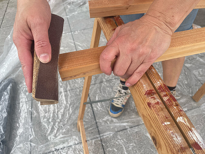 Grillplatz für die Terrasse bauen: Glätten der zugeschnittenen Holzlatte mit Schleifklotz – wichtiger Arbeitsschritt für saubere Kanten und eine sichere Verarbeitung beim Bau der DIY-Grillstation.
