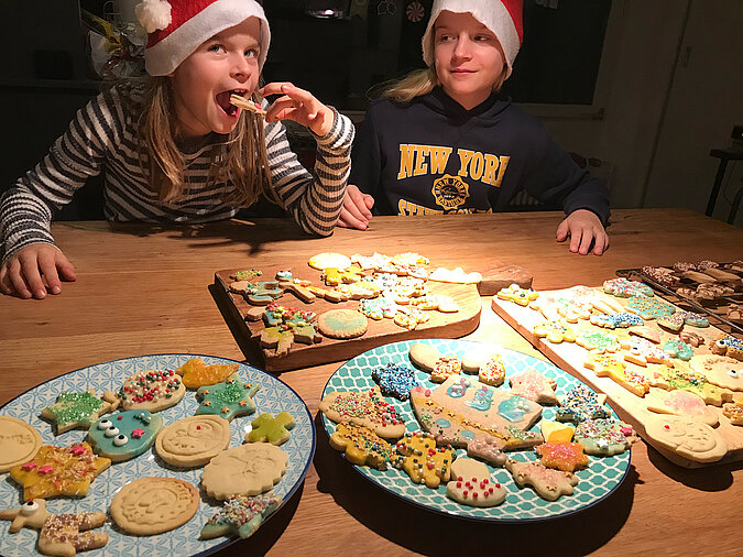 Lernturm für Kinder bauen und fröhliches gemeinsames Plätzchenbacken mit bunt dekorierten Weihnachtskeksen, Kindern beim Ausstechen und Verzieren am Küchentisch