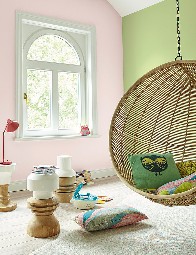 Kinderzimmer mit rosa und grüner Wand und Hängesessel aus Korb