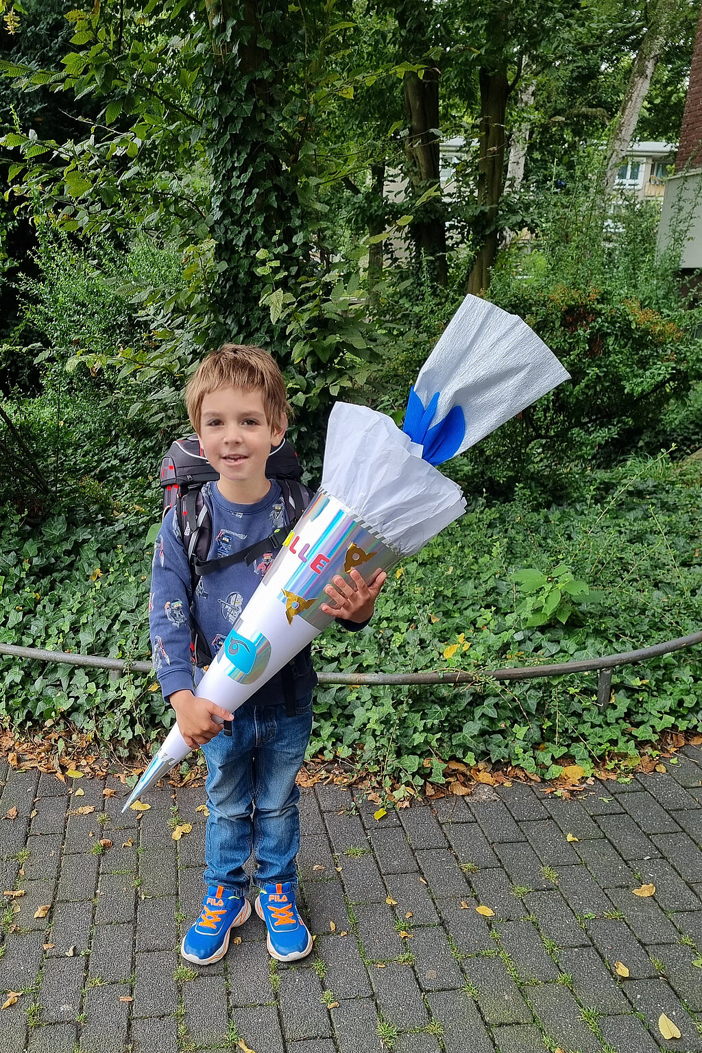 Junge steht mit einer Ninjago-Schultüte im Arm vor einer Hecke