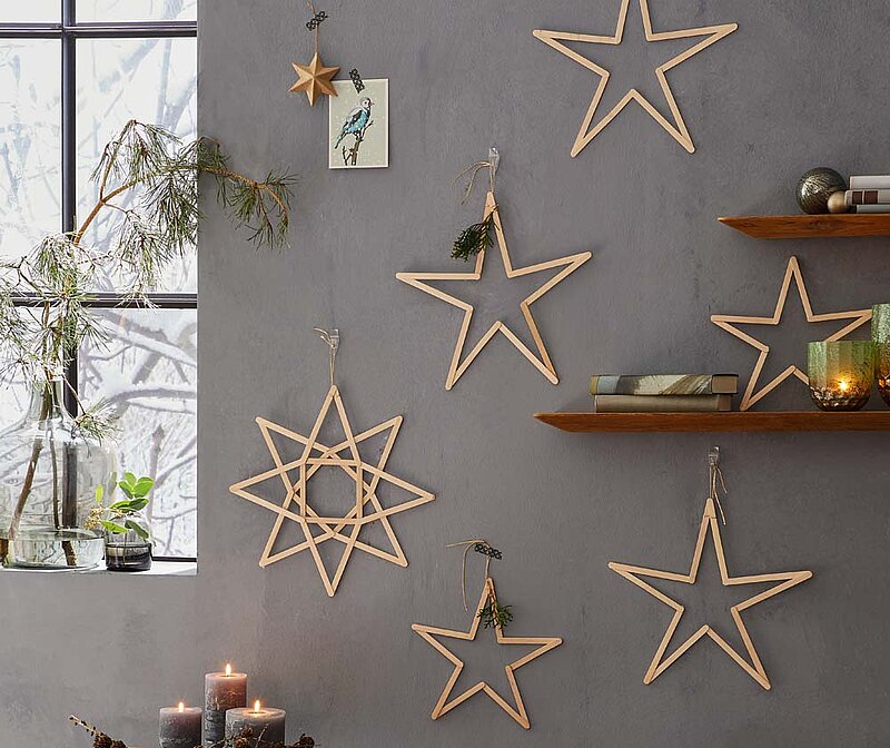festliche Sterne aus Holzstielen hängen an einer dunkelgrauen Wand