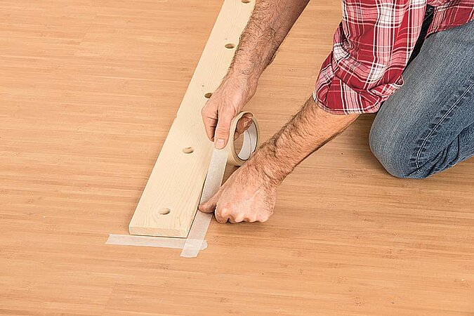 Unteres Holzbrett für den Raumteiler aus Birkenstämmen wird mit Klebeband auf dem Boden fixiert