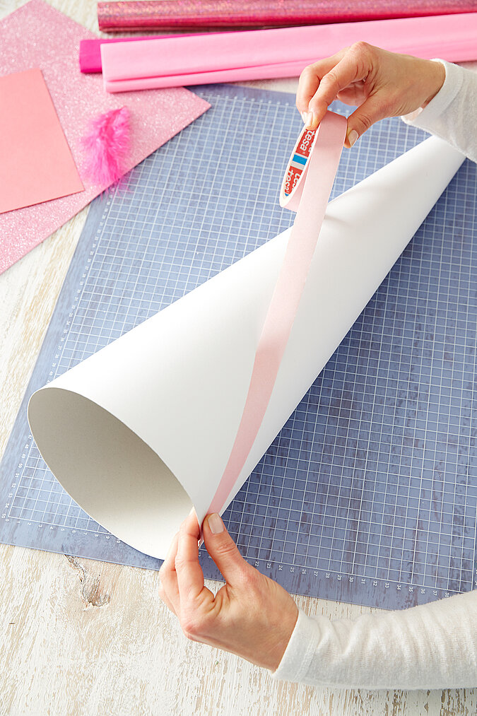 Auf einen weißen Schultüten-Rohling werden rosa Malerkrepp-Streifen für den Einhorn-Look geklebt
