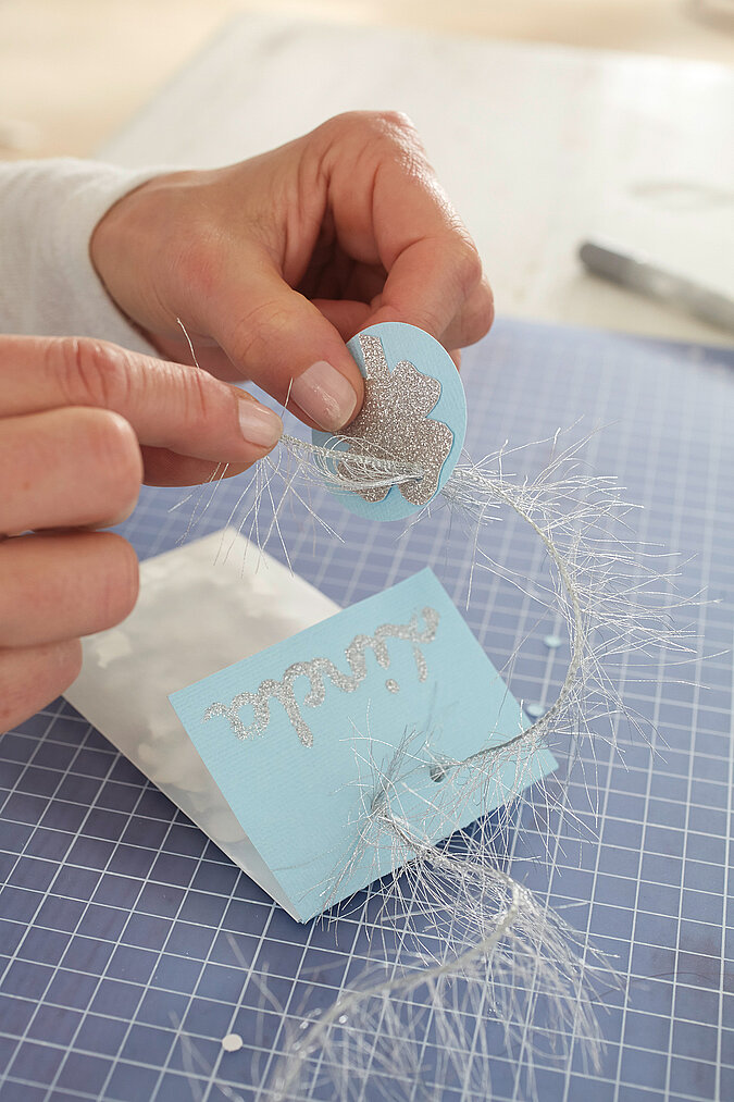 Der Glückskleeanhänger wird mit Glitzerfaden an das Konfettitütchen gebunden