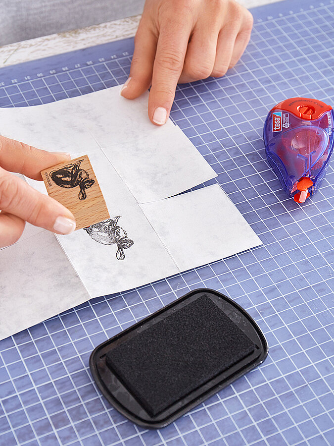 Hasenmotiv wird mit Holzstempel auf marmoriertes Papier gestempelt, daneben liegen Stempelkissen und tesa Kleberoller