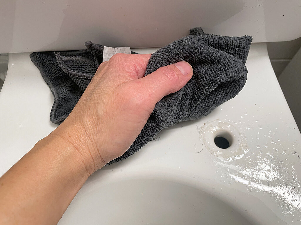 Klodeckel wechseln & pflegen – Demontage des alten Klodeckels, Hand mit Microfasertuch reinigt Kloschüssel