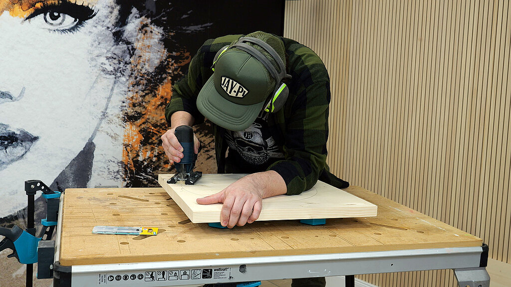 Mann saegt mit der Stichsaege runde Tischplatte aus quadratischer Holzplatte aus