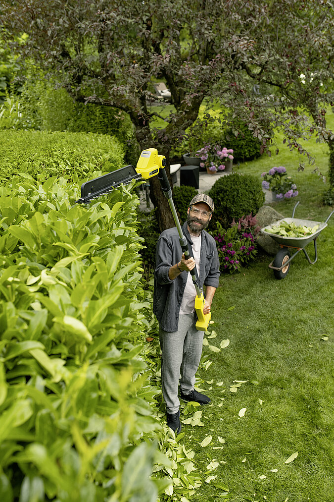 Gartenarbeiten Frühling: Hohe Gartenhecke mit elektrischer Teleskop-Heckenschere sicher und gleichmäßig schneiden