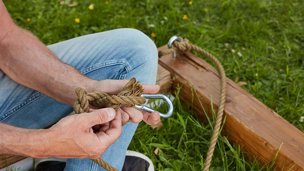 Mann verknotet ein Seil am Karabinerhaken
