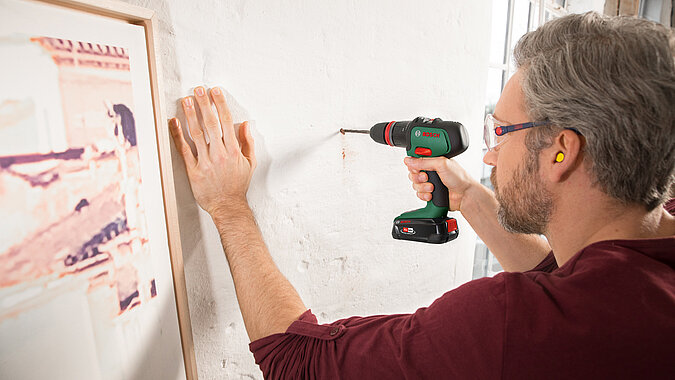 Mann bohrt mit Akkuschrauber loch für ein Bild an die Wand zum Aufhängen