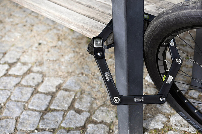 Mythen über richtigen Einbruchschutz – Fahrrad wird mit stabilem Faltschloss sicher an festem Gegenstand abgeschlossen