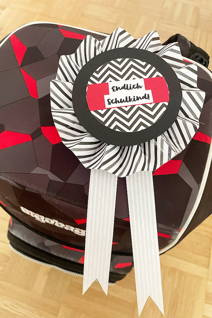 Einschulung Orden basteln mit schwarz weißer Papierrosette am Schulranzen befestigt