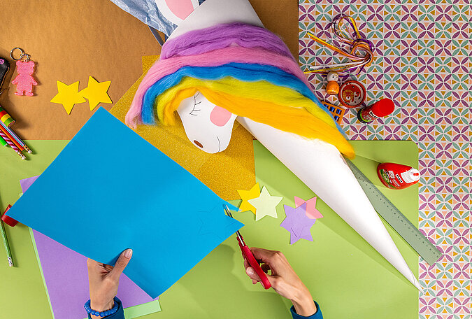 Schultüte Einhorn basteln beim Ausschneiden von bunten Sternen aus Bastelpapier