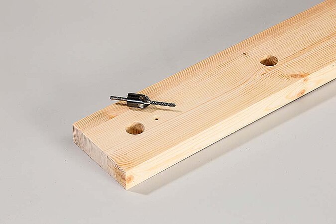 Vorgebohrtes Holzbrett mit Bohrer für einen Raumteiler aus Birkenstämmen liegt auf einer Werkbank