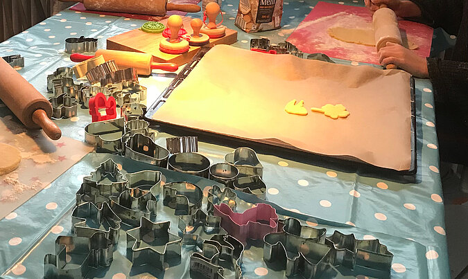 Lernturm für Kinder bauen und gemeinsam fantasievoll ausgestochene Weihnachtskekse dekorieren, bunte Plätzchen auf Backblechen und Arbeitsfläche verteilt