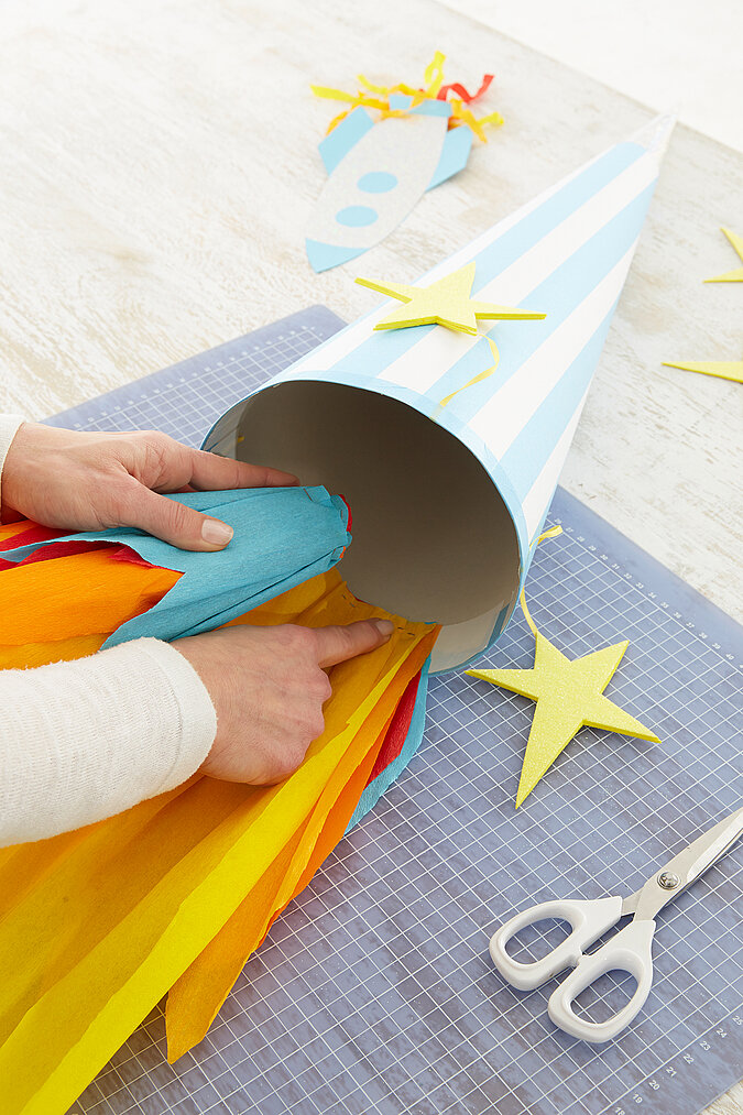 An einer Schultüte wird an der Öffnung ein guter Krepppapierstreifen im Flammen-Look angeklebt
