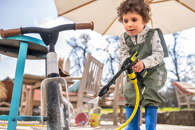 Tipps zum Heimwerken mit Kindern: Junge säubert mit einem Kinder-Reinigungsgerät ein Laufrad