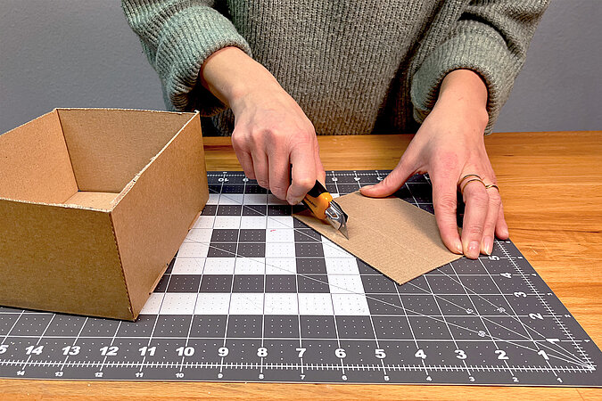 Mit einem Cuttermesser werden schmale Streifen aus einer pappe zugeschnitten
