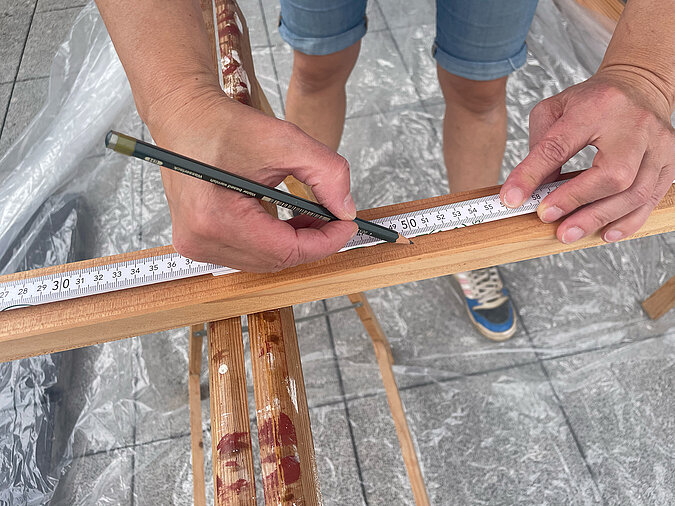 Grillplatz für die Terrasse bauen: Exaktes Anzeichnen von Konstruktionsholz mit Zollstock und Bleistift als Vorbereitung für den DIY-Zuschnitt beim Bau einer Grillstation auf der Terrasse.