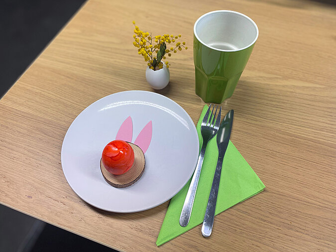 Osterkranz aus Eierschalen basteln mit kreativ gedecktem Ostertisch, rotem Ei mit Hasenohren auf Teller und frühlingshafter Tischdeko